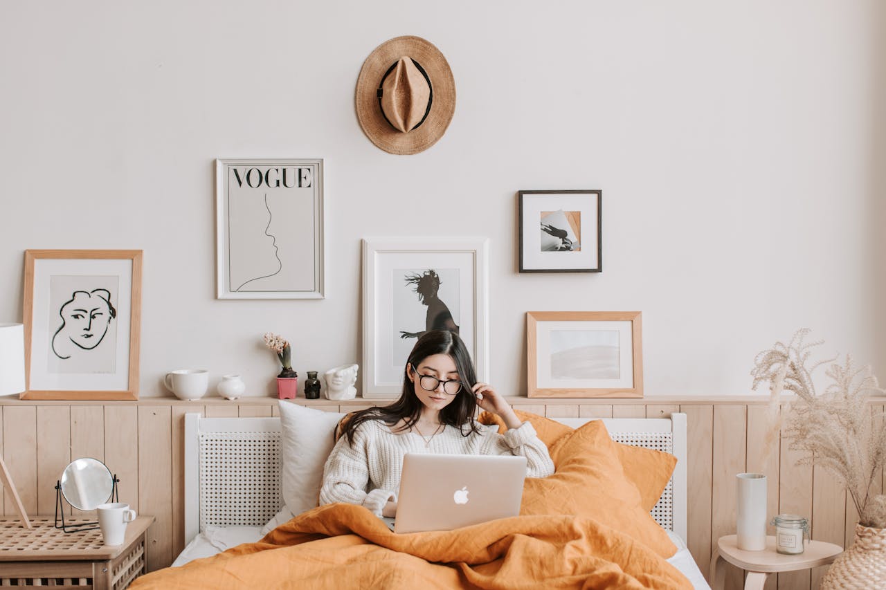 Young woman working on a laptop from bed in a cozy, stylish room, representing flexibility and the best online jobs for students.