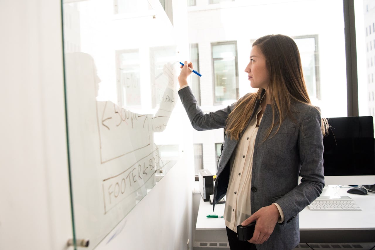 Professional woman demonstrating soft skills by writing on a whiteboard in a modern office, showcasing collaboration, communication, and problem-solving.