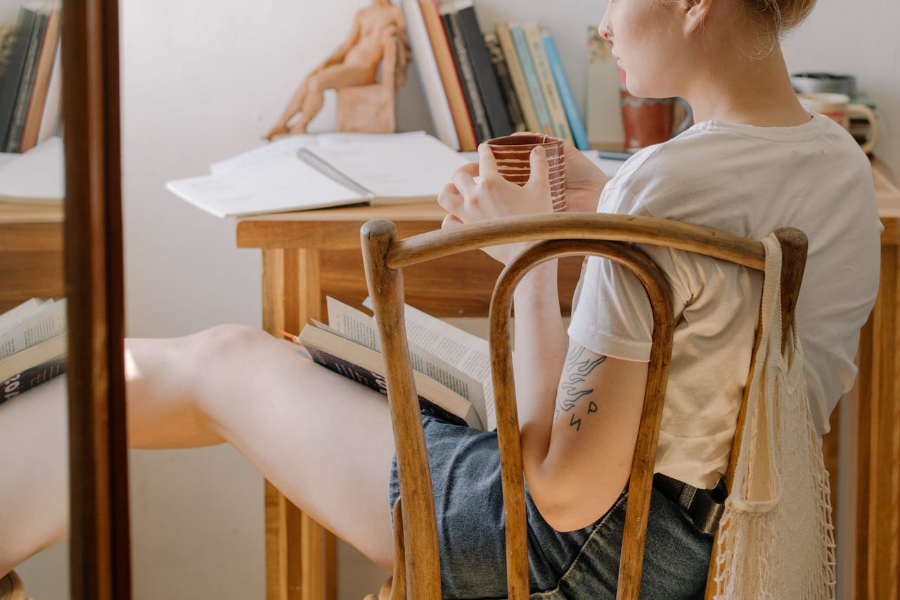 A university student relaxing with a book and a cup of coffee in a cosy dorm room, enjoying some quiet time as one of many affordable treats on a student budget.